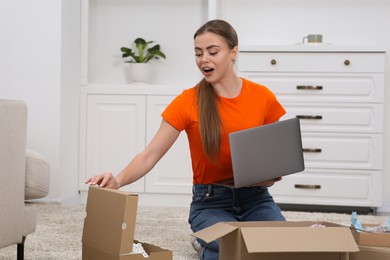 Photo of Emotional woman with laptop unpacking parcels at home. Online store