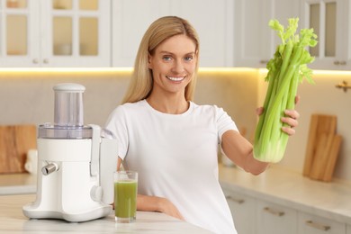 Photo of Happy woman with fresh celery bunch at table in kitchen