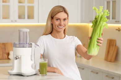 Happy woman with fresh celery bunch at table in kitchen