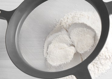 Sieve and flour on white wooden table, closeup