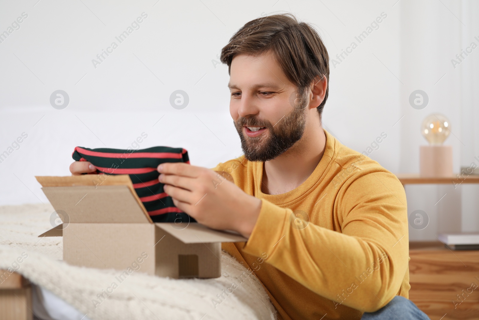 Photo of Happy man opening parcel at home. Internet shopping