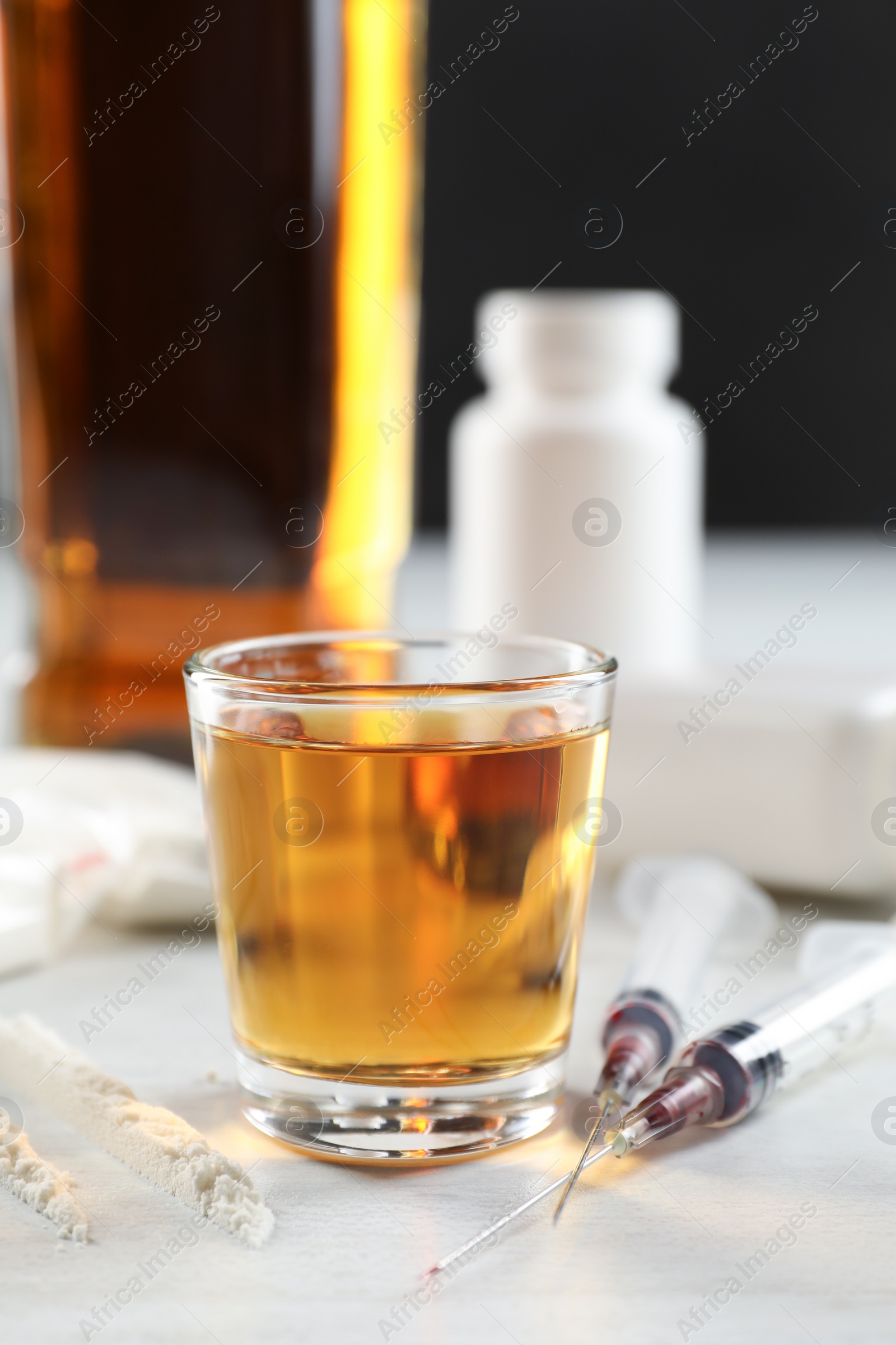 Photo of Alcohol and drug addiction. Whiskey in glass, syringes and cocaine on white table