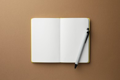 Open notebook with blank pages and pen on light brown background, top view. Space for text