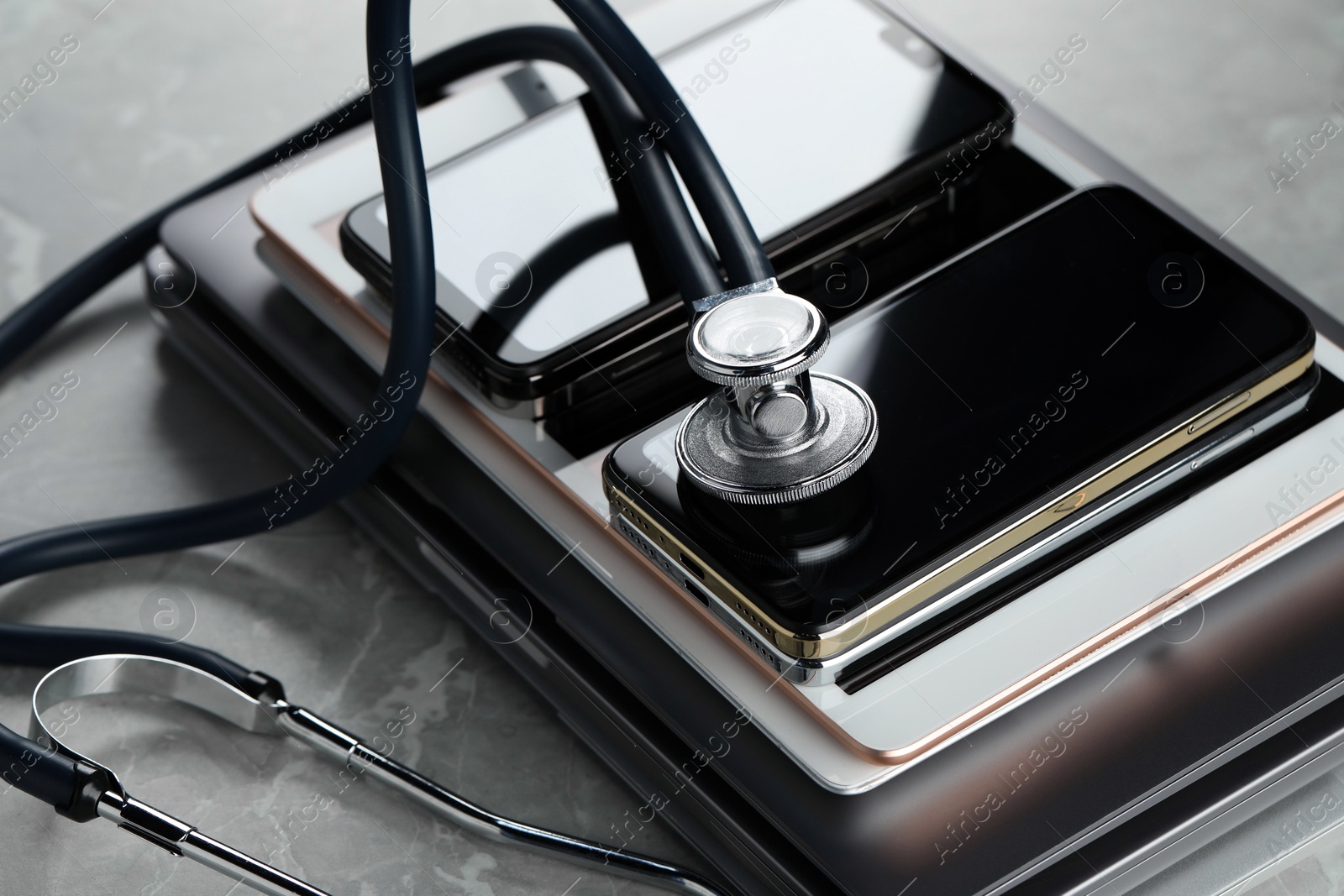 Photo of Stack of electronic devices and stethoscope on grey table, closeup