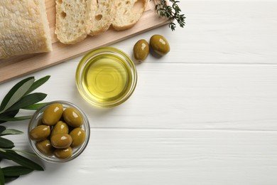 Bowl of cooking oil, ripe olives and bread on white wooden table, flat lay. Space for text