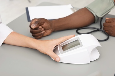 Young doctor checking African-American patient's blood pressure in hospital