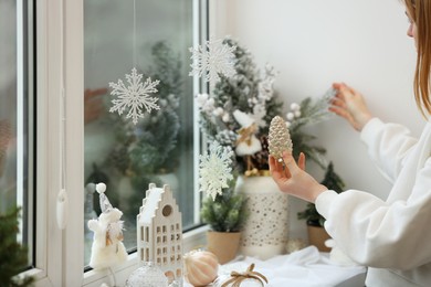 Woman holding Christmas bauble in shape of cone near window sill indoors, closeup