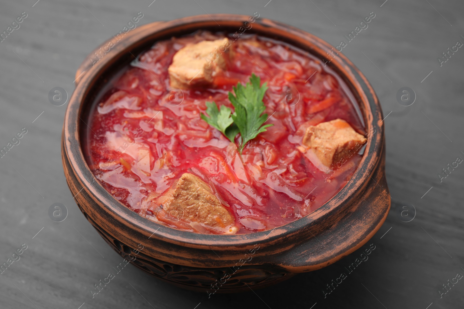 Photo of Tasty borscht in bowl on grey wooden table, closeup