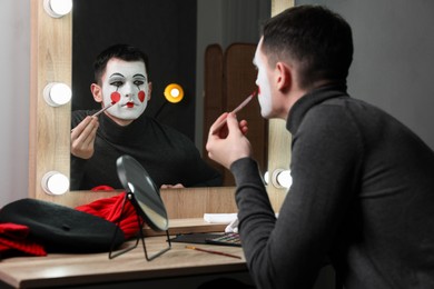 Photo of Young man applying mime makeup near mirror in dressing room