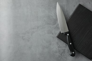 Photo of Knife and black wooden board on grey textured table, top view. Space for text