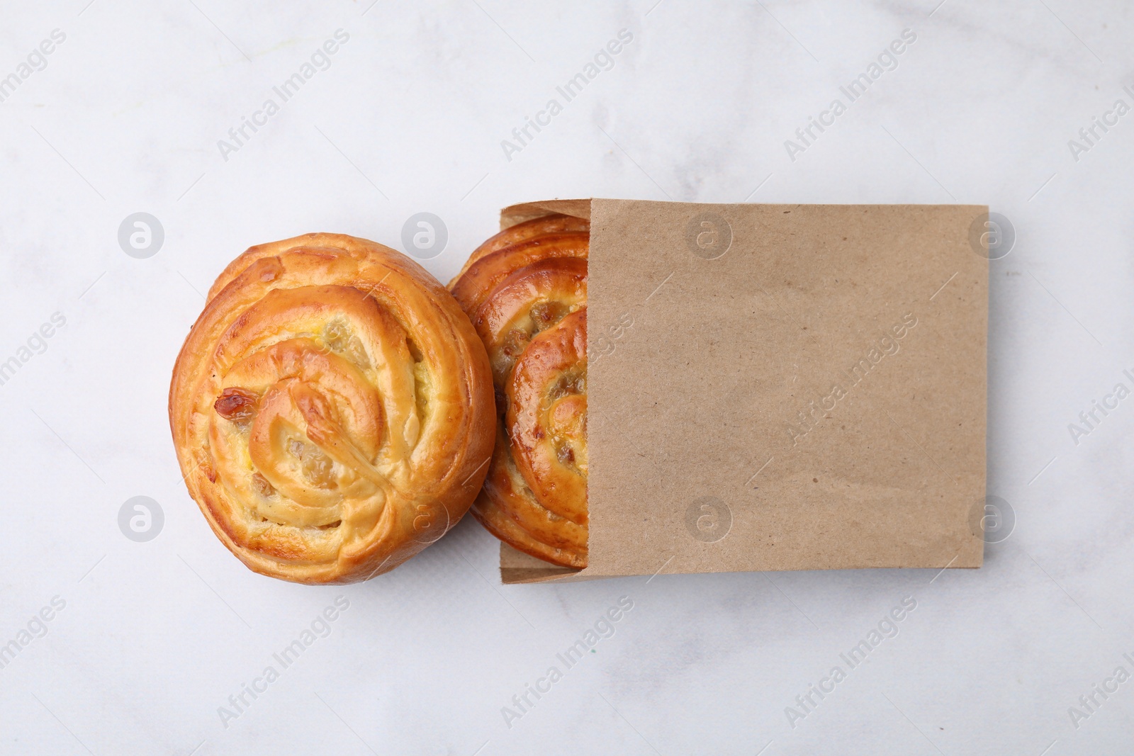 Photo of Paper bag with delicious rolls on white marble table, top view. Sweet buns