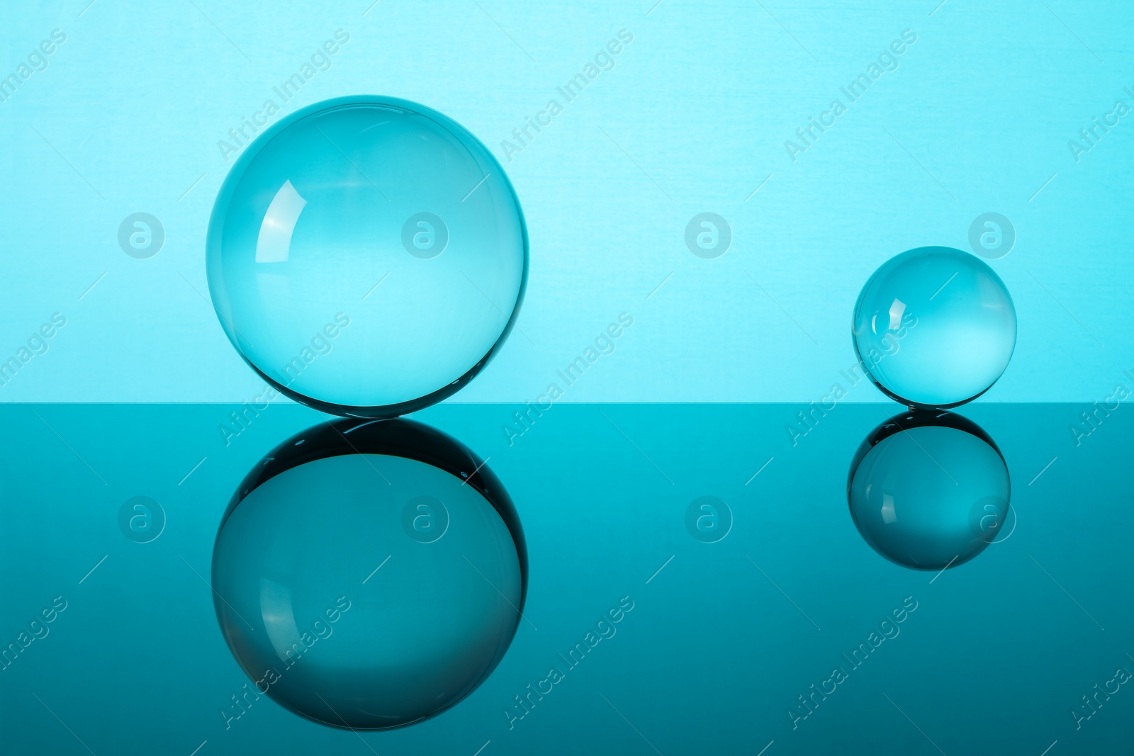 Photo of Transparent glass balls on mirror surface against turquoise background