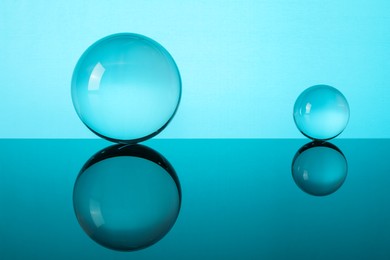 Photo of Transparent glass balls on mirror surface against turquoise background