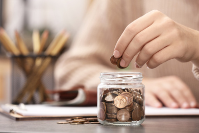 Photo of Woman putting money into glass jar at table, closeup