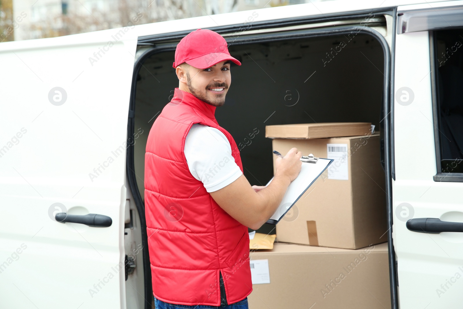 Photo of Young courier checking amount of parcels in delivery van, outdoors