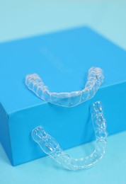 Photo of Transparent dental aligners on light blue background, closeup