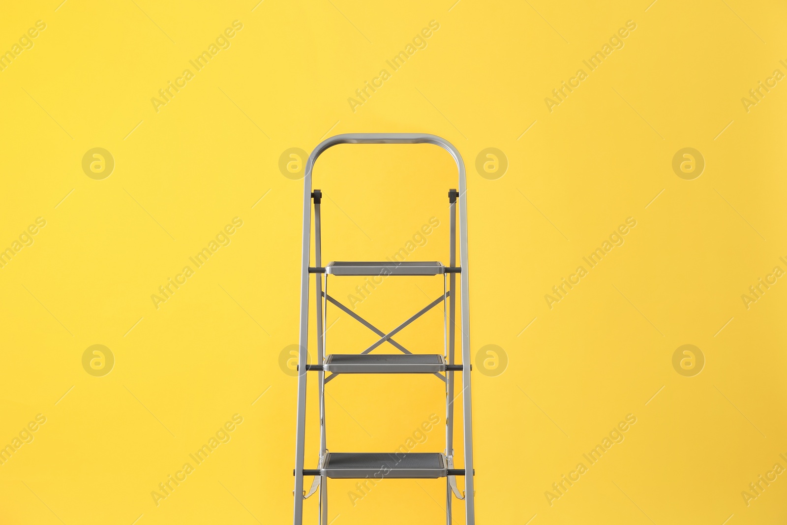 Photo of Modern metal stepladder on yellow background. Construction tool