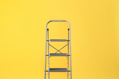Photo of Modern metal stepladder on yellow background. Construction tool