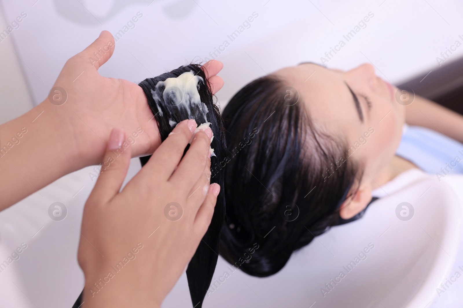 Photo of Professional hairdresser applying conditioner on woman's hair in beauty salon, closeup