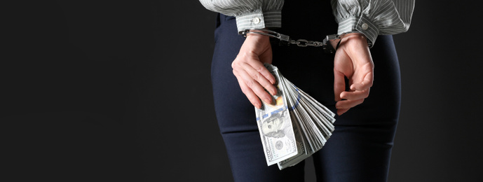 Woman in handcuffs holding bribe on black background, closeup. Banner design