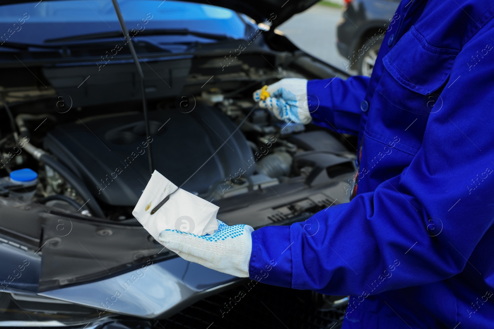 Photo of Worker checking motor oil level in car with dipstick, closeup