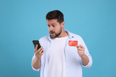 Photo of Scared man with credit card and smartphone on light blue background. Be careful - fraud