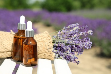 Bottles of essential oil and lavender flowers on white wooden surface outdoors, space for text