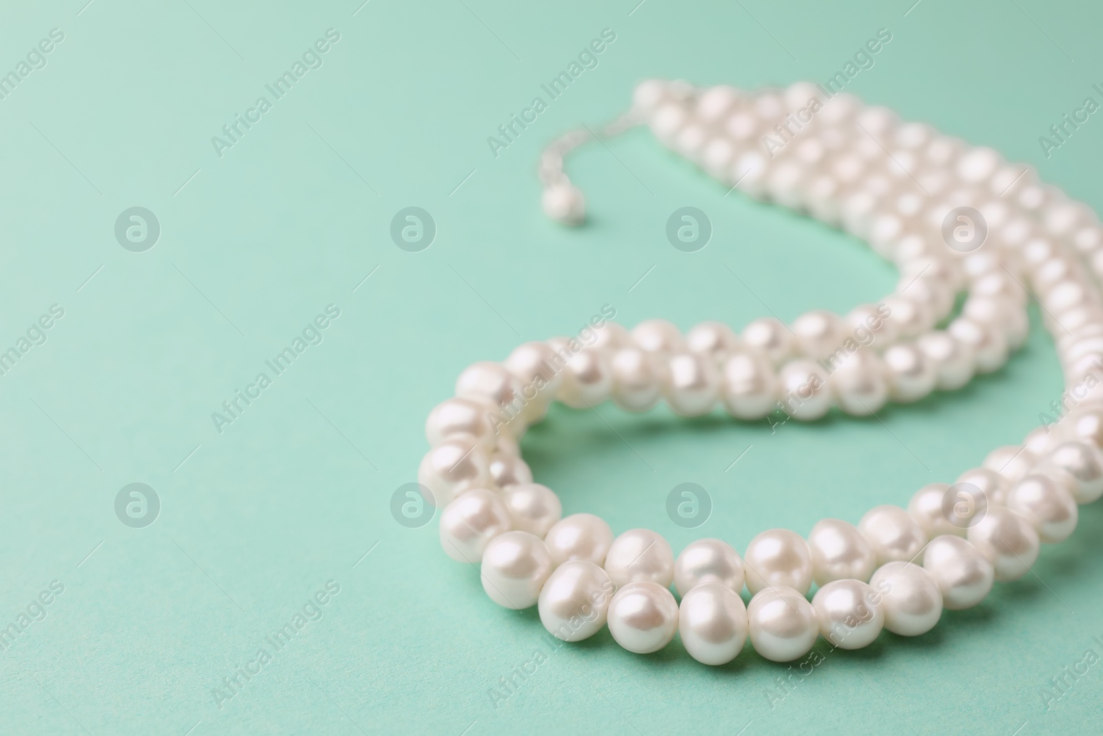 Photo of Elegant pearl necklace on turquoise background, closeup. Space for text