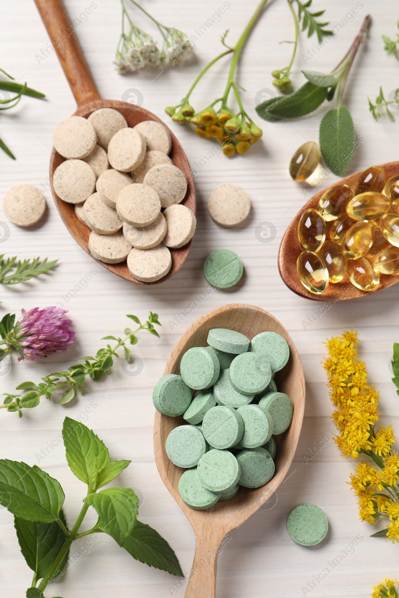 Photo of Different pills, herbs and flowers on white wooden table, flat lay. Dietary supplements