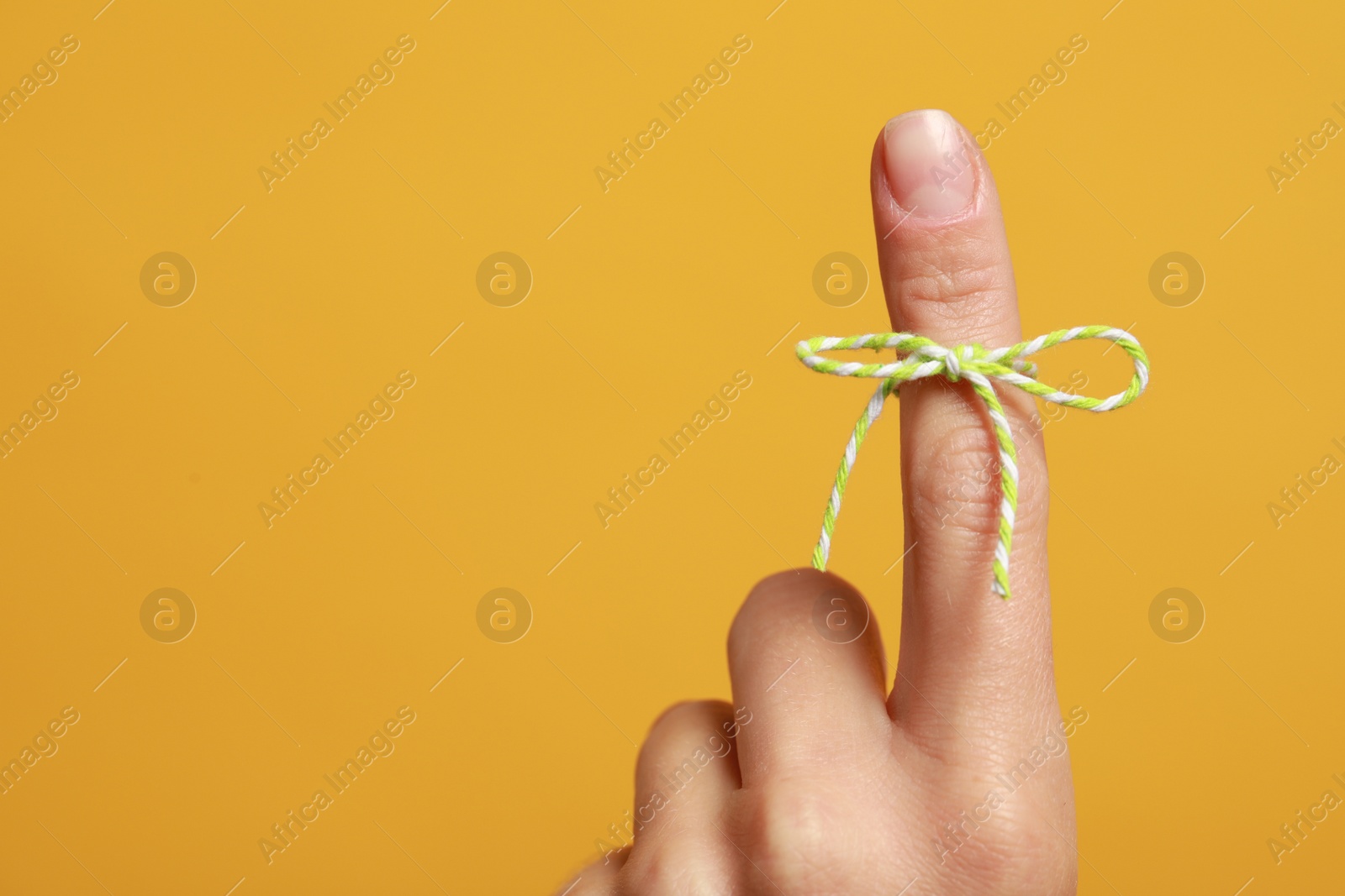 Photo of Woman showing index finger with tied bow as reminder on orange background, closeup. Space for text
