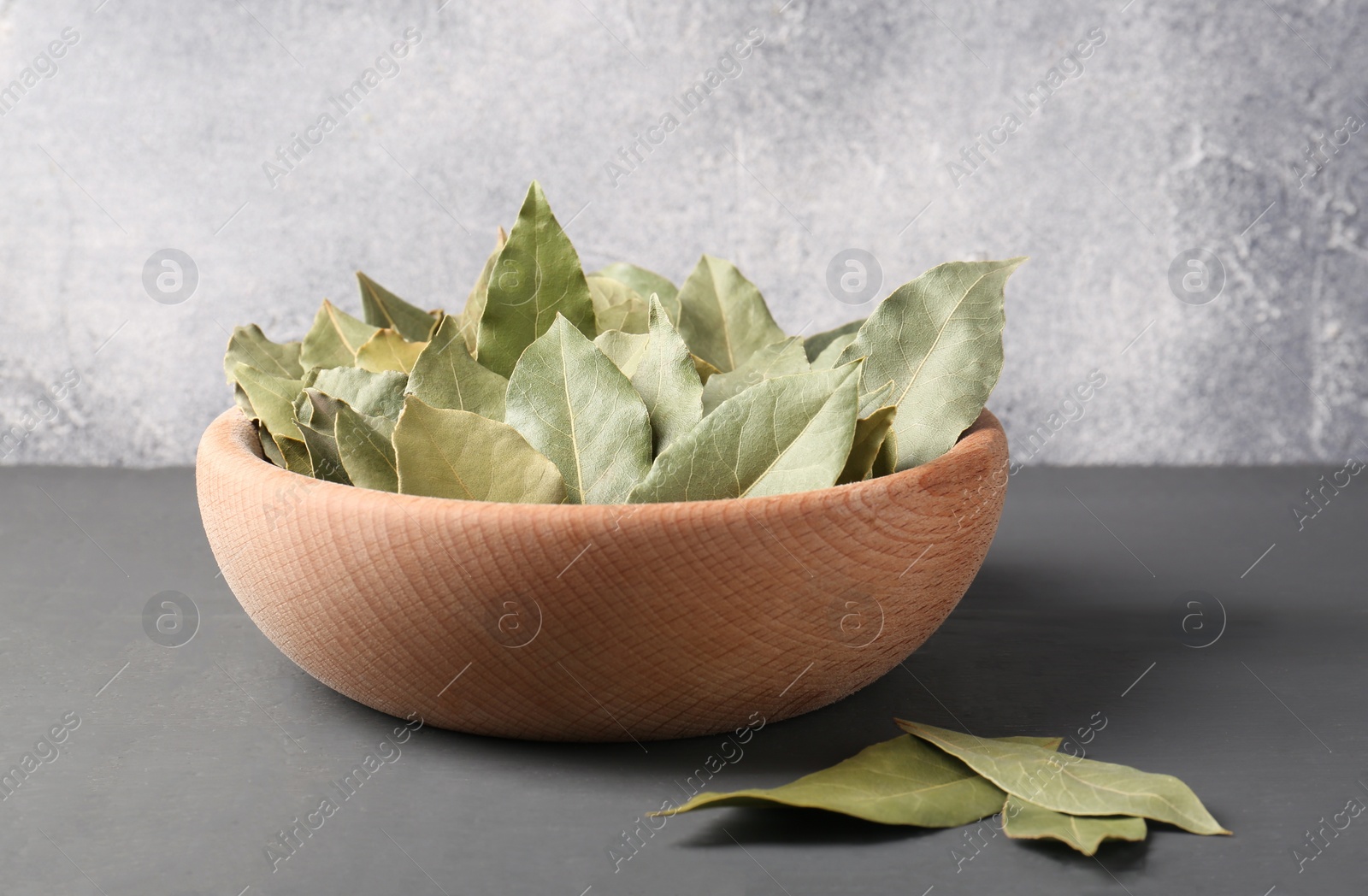 Photo of Aromatic bay leaves in wooden bowl on gray table