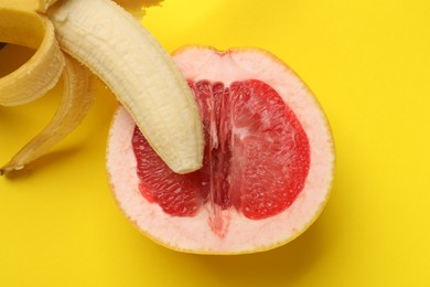 Photo of Banana and half of grapefruit on yellow background, top view. Sex concept