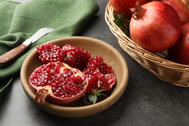 Photo of Fresh pomegranates, green leaves and knife on grey table