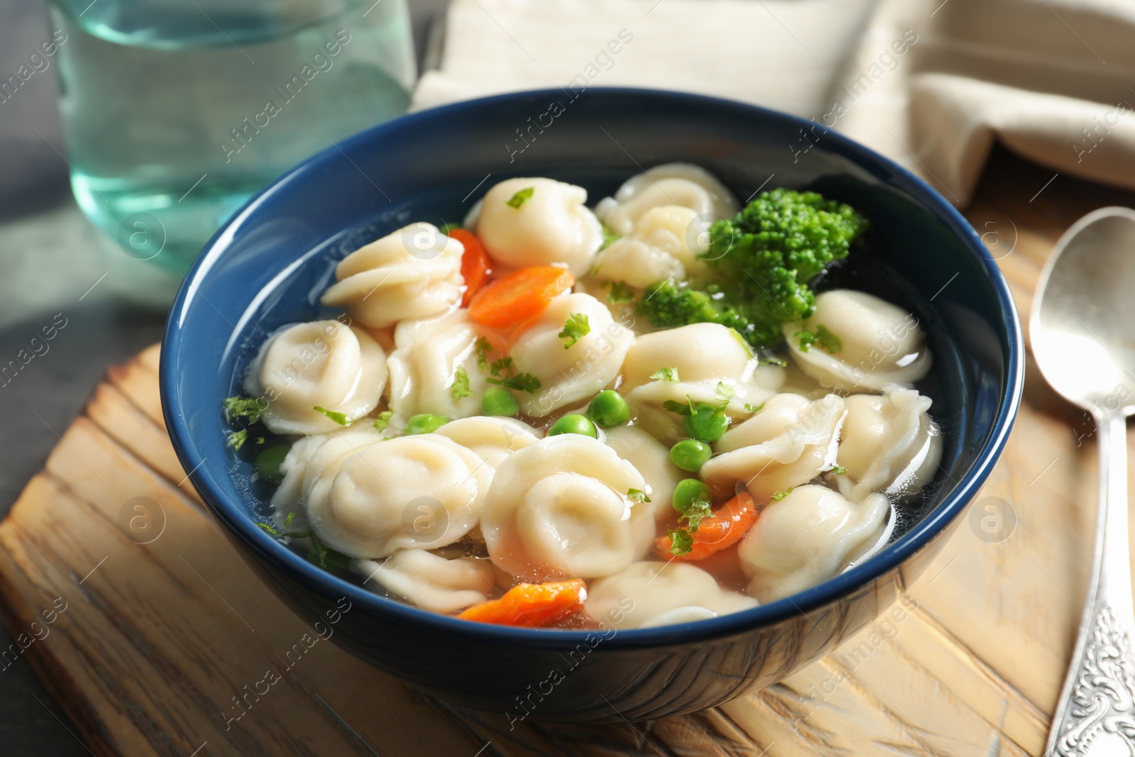 Photo of Board with bowl of dumplings in broth and spoon on table