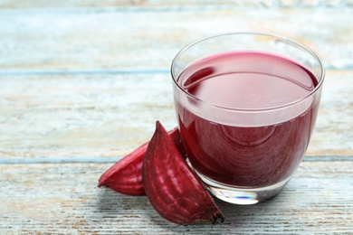 Photo of Cut beet and glass of juice on blue wooden table. Space for text