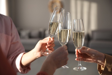 Photo of People clinking glasses of champagne in living room, closeup. Holiday cheer and drink