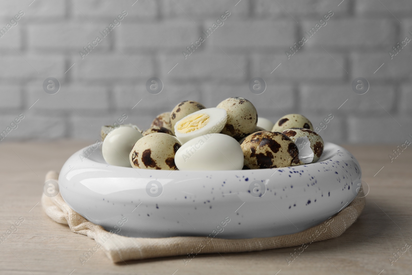 Photo of Unpeeled and peeled hard boiled quail eggs in bowl on white wooden table, closeup