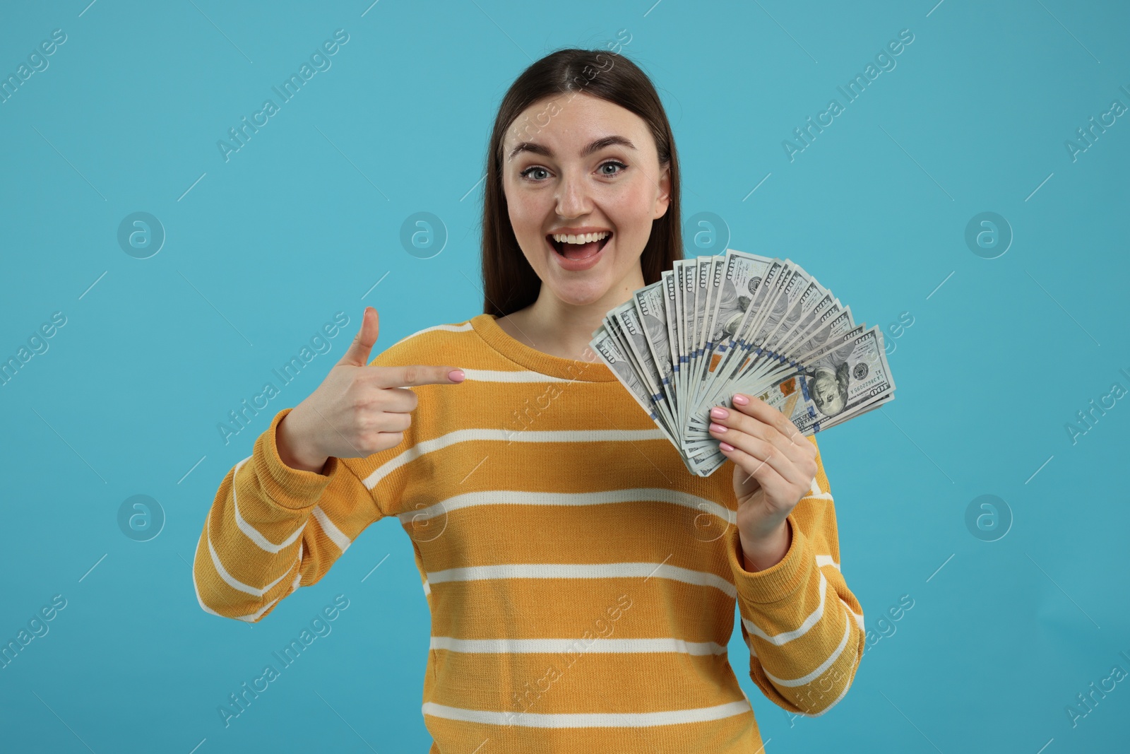 Photo of Happy woman pointing at dollar banknotes on light blue background