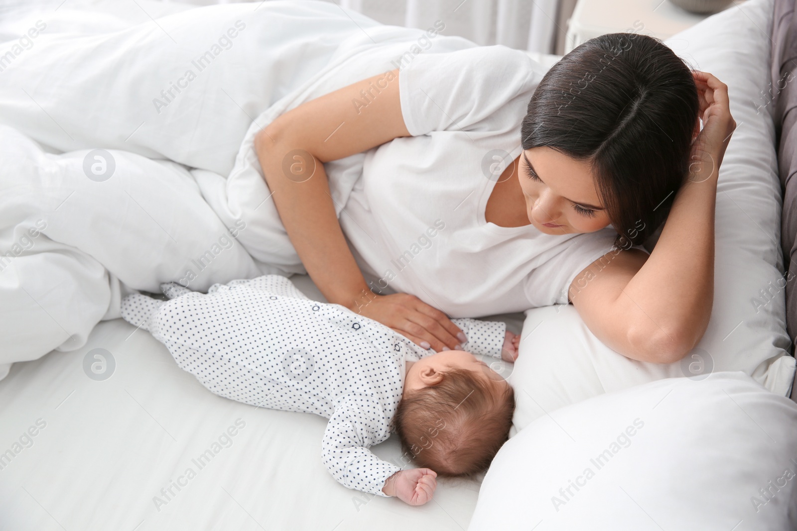 Photo of Happy woman with her sleeping baby on bed