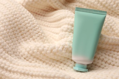 Photo of Winter skin care. Hand cream on white knitted cloth, closeup. Space for text