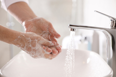 Man washing hands with soap over sink in bathroom, closeup