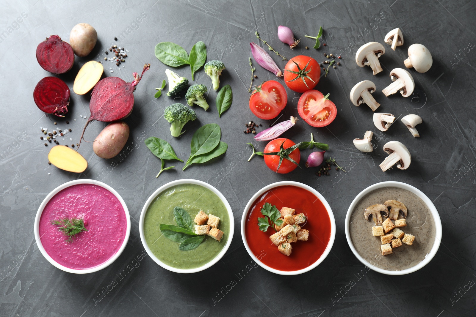 Photo of Different tasty cream soups in bowls and ingredients on dark grey table, flat lay