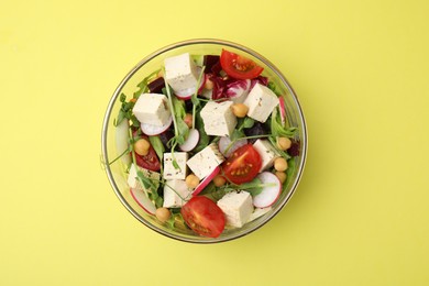 Bowl of tasty salad with tofu and vegetables on yellow background, top view