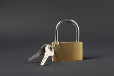 Photo of Steel padlock with keys on dark grey background, closeup