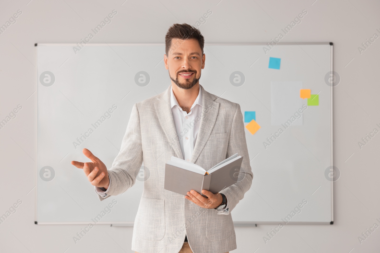 Photo of Happy teacher with book explaining something at whiteboard in classroom