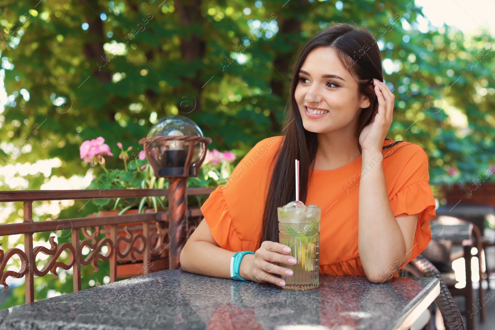 Photo of Young woman with glass of tasty lemonade at table in cafe, outdoors. Natural detox drink