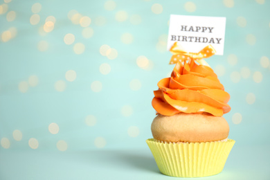 Beautiful birthday cupcake on light blue background with blurred lights. Space for text