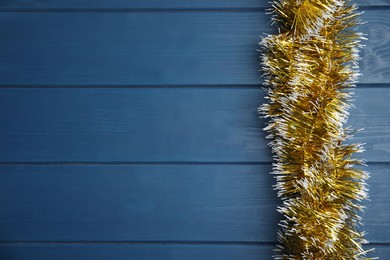 Golden tinsel on blue wooden background, top view. Space for text