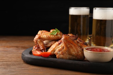 Photo of Mugs with beer, delicious baked chicken wings and sauce on wooden table