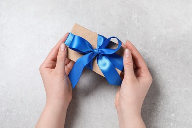 Woman holding gift box with blue bow at light grey table, top view